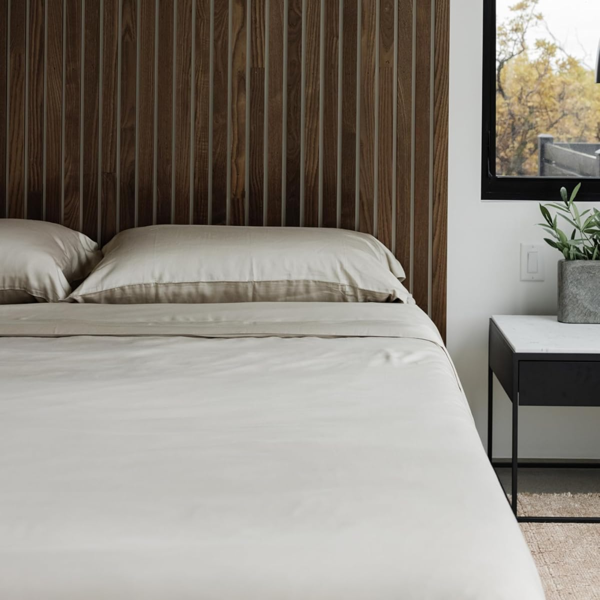 a bed with taupe sheets and pillows and a wood paneled headboard