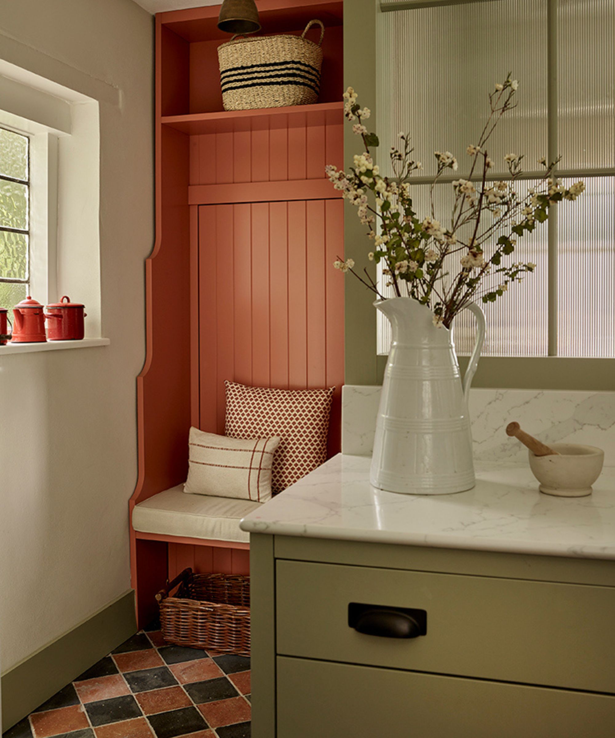 a small cottage kitchen painted in pale green with a quarry floor and a tiny red entryway bench area