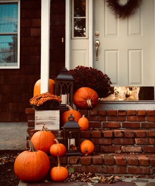 Halloween door decor ideas with pumpkins and lanterns running down steps to one side, and brown wreath of dried branches on the door