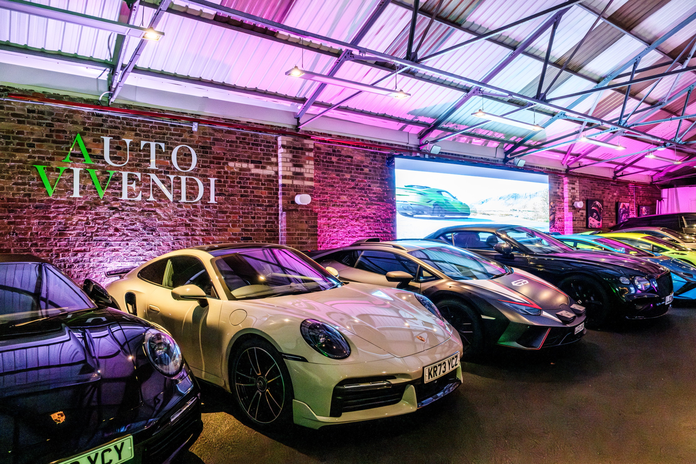 View of the interior of the Auto Vivendi warehouse. It's lit in purple and there are lots of cars