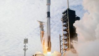 a tall, black and white rocket lifts off into a mostly cloudy sky from a Florida launch pad