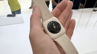 En hand som håller upp en vit Apple Watch SE 2 och visar dess sensorer på baksidan.