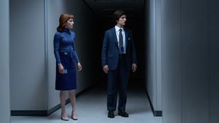 Britt Lower in a blue dress as Helly and Adam Scott in a suit as Mark stand in a corridor in Severance.