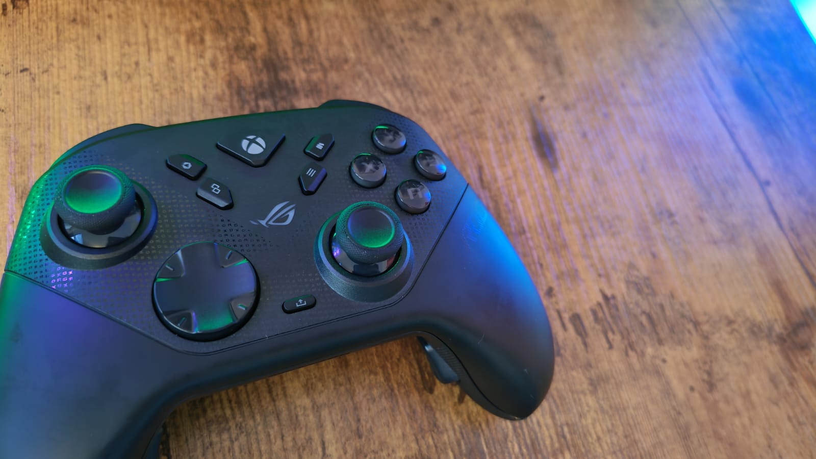 An Asus ROG Raikiri 2 controller to the left, on a wooden desk surface