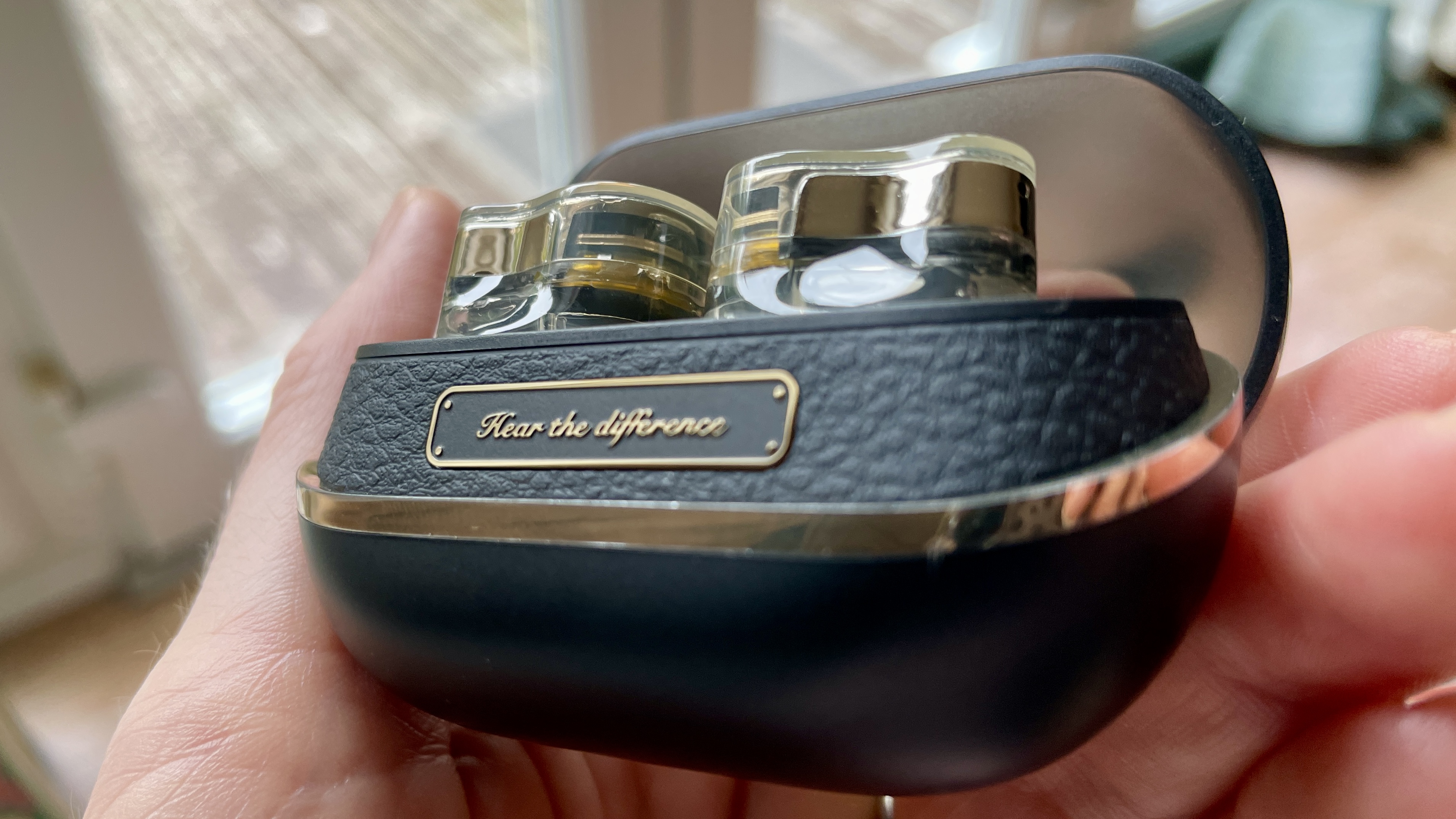 SoundPeats H3 earbuds and case held in a hand, in a living room