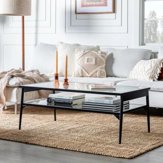 Black metal coffee table with glass top and glass shelf sitting on jute rug in white living room