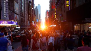 Crowds of people in Times Square with the sun setting between the buildings