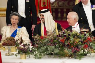 Princess Anne laughs while wearing a cream dress with a royal blue sash and a delicate tiara as she attends the Qatari State Dinner at Buckingham Palace