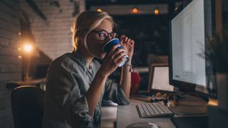 Woman sat at her laptop at night drinking coffee