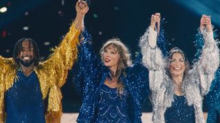 Taylor Swift holding hands with two of her dancers and lifting their arms up at the end of the Karma performance during The Eras Tour.