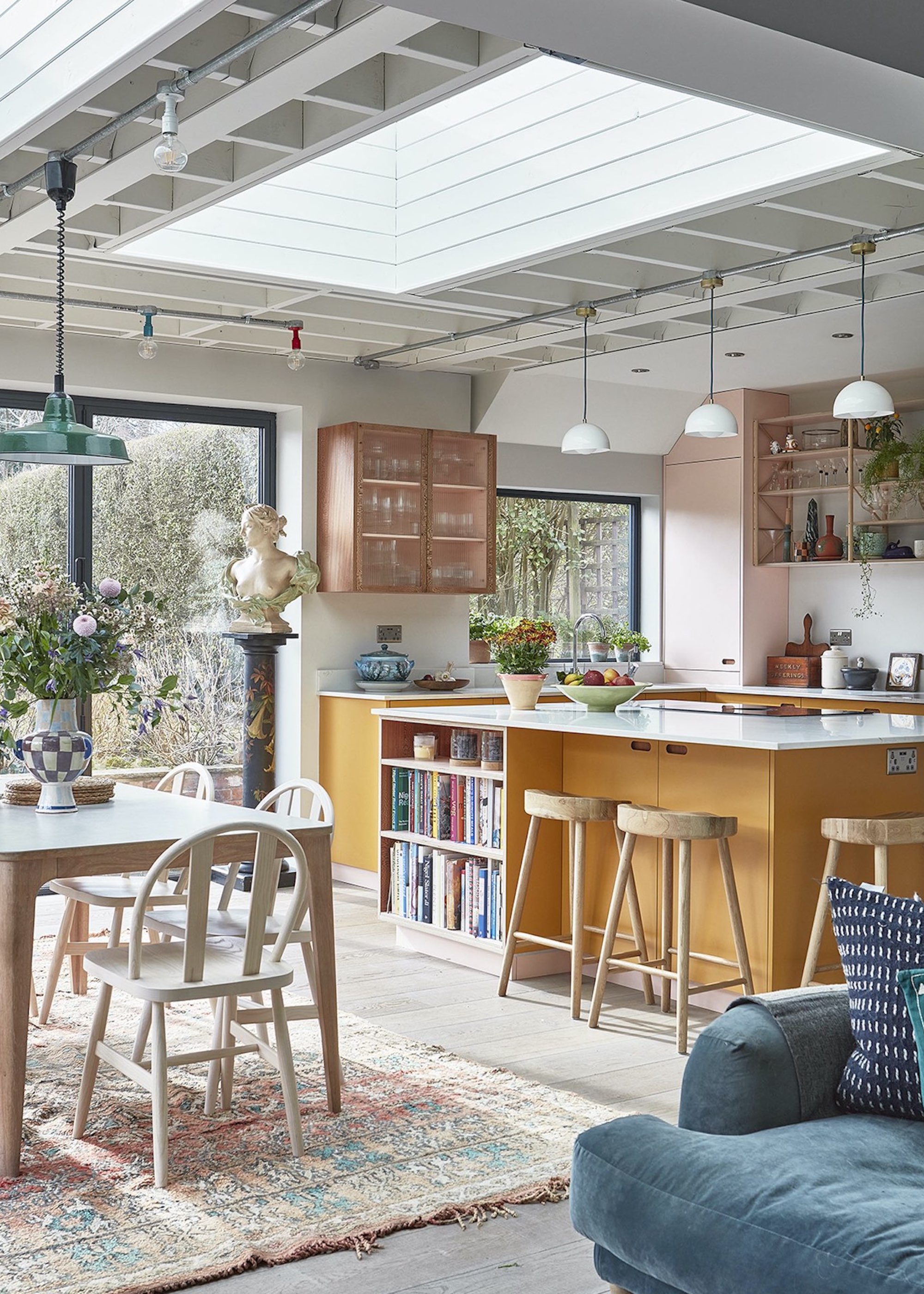 A bright kitchen extension with an orange kitchen island and an oak colored dining table in the middle of an open plan space.