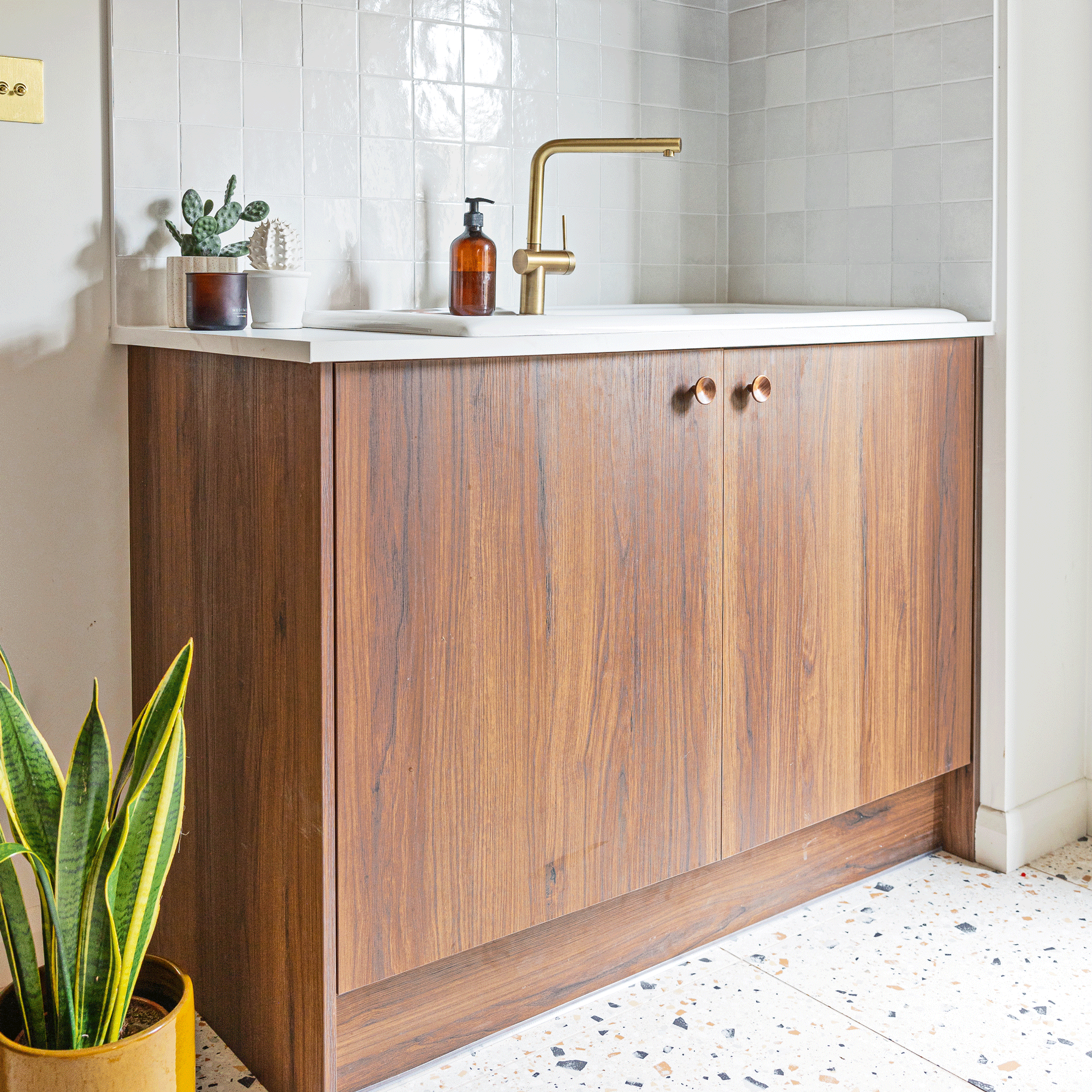 a small utility room area with sink, dark wood cabinet and white tiles