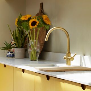 a gold coloured hot water kitchen tap in a yellow kitchens with a vase of sunflowers