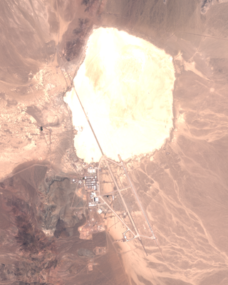 a dry lake bed seen from space. an installation of buildings and runways sits next to it