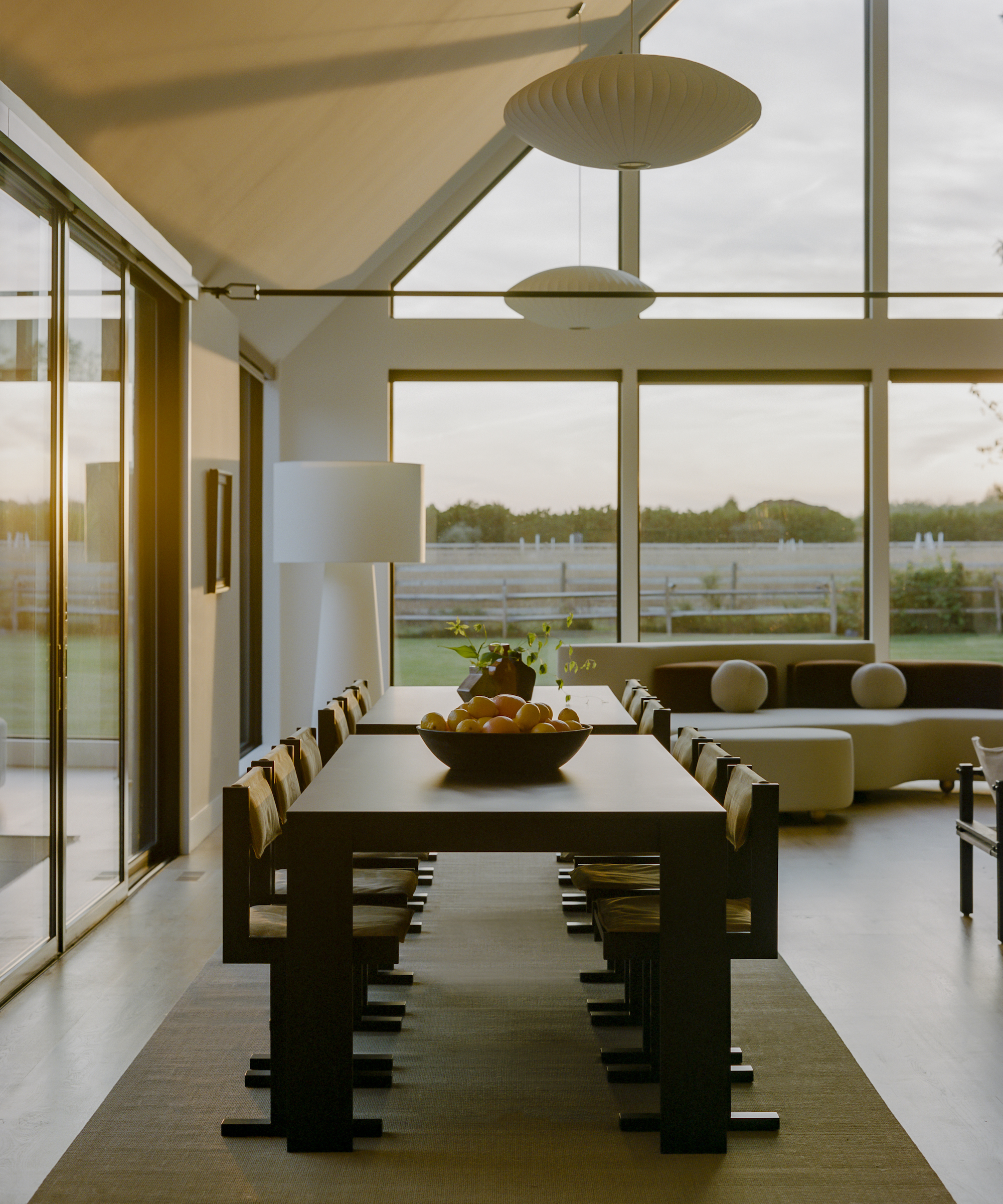 Living dining room with large wood dining table on area rug, pendant lights above and large floor lamp beyond, and white curved sofa beyond