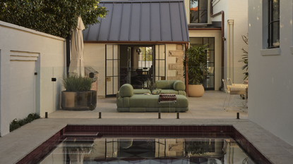 Rear garden of Smac Studio's renovated Art Deco home, featuring a pink checkerboard pool, lush mature trees and contemporary outdoor living spaces that seamlessly connect with the house.