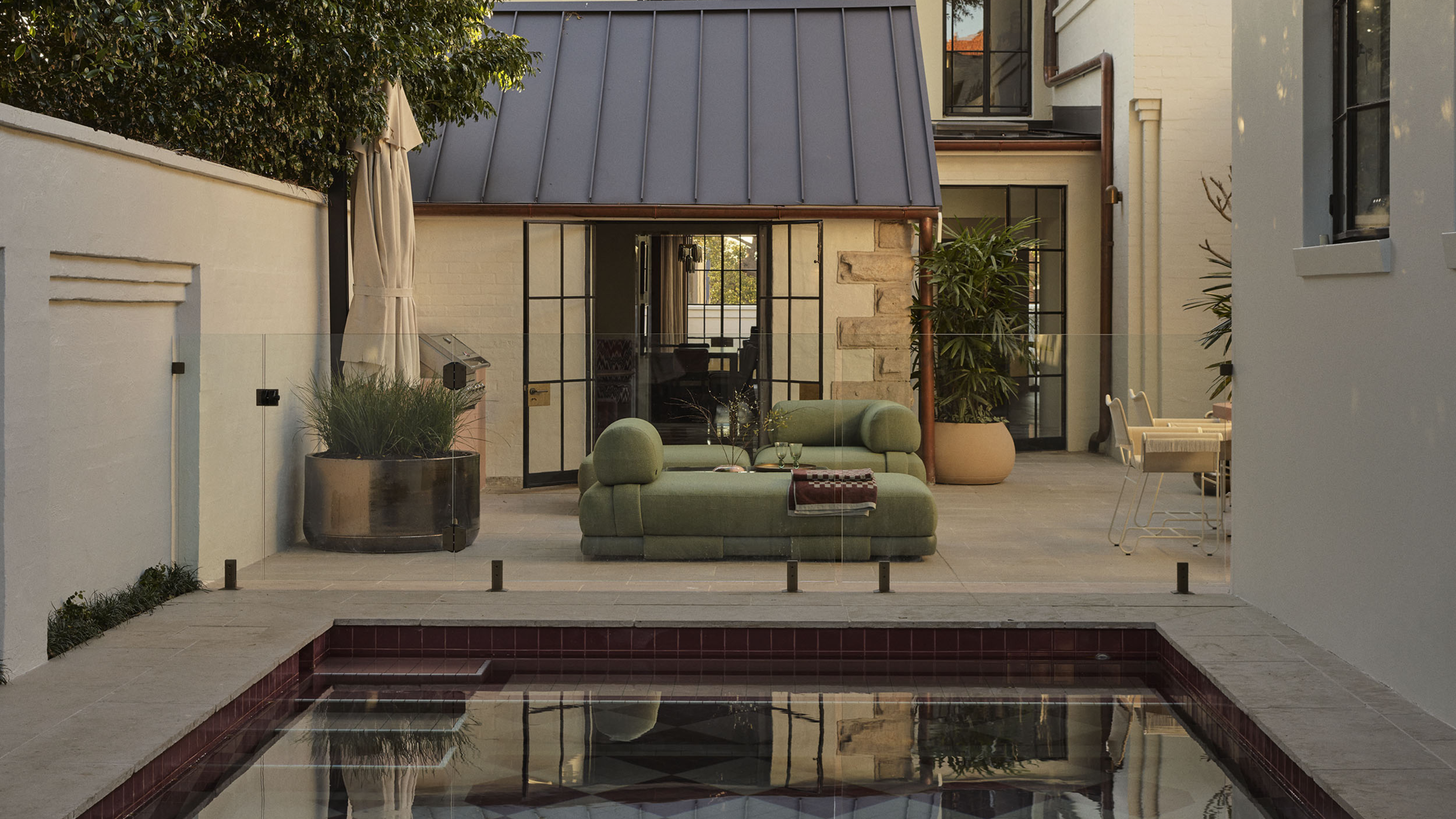 Rear garden of Smac Studio's renovated Art Deco home, featuring a pink checkerboard pool, lush mature trees and contemporary outdoor living spaces that seamlessly connect with the house.
