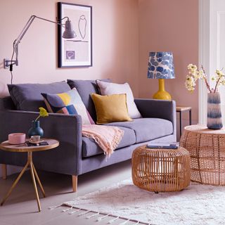 A pink living room with a blue sofa and rattan tables