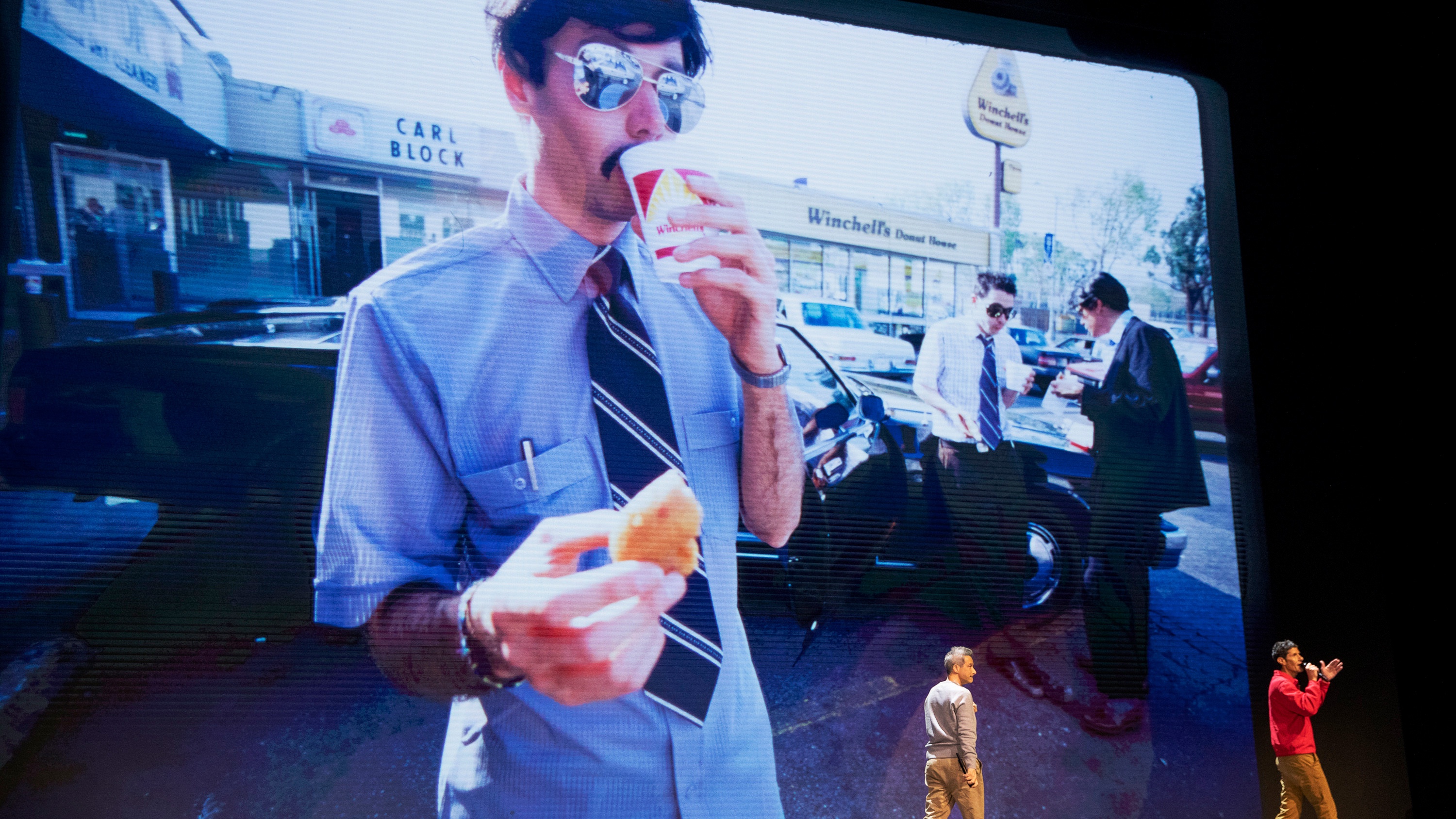 A still from the Beastie Boys Story, with AdRock and Mike D talking in front of an image of MCA from the Sabotage video