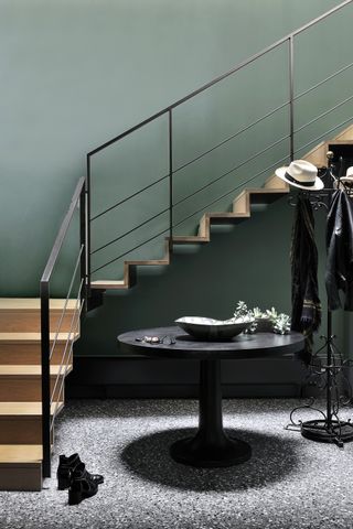 Wooden staircase with black metal bannister, circular table and coat rack on the grey flooring