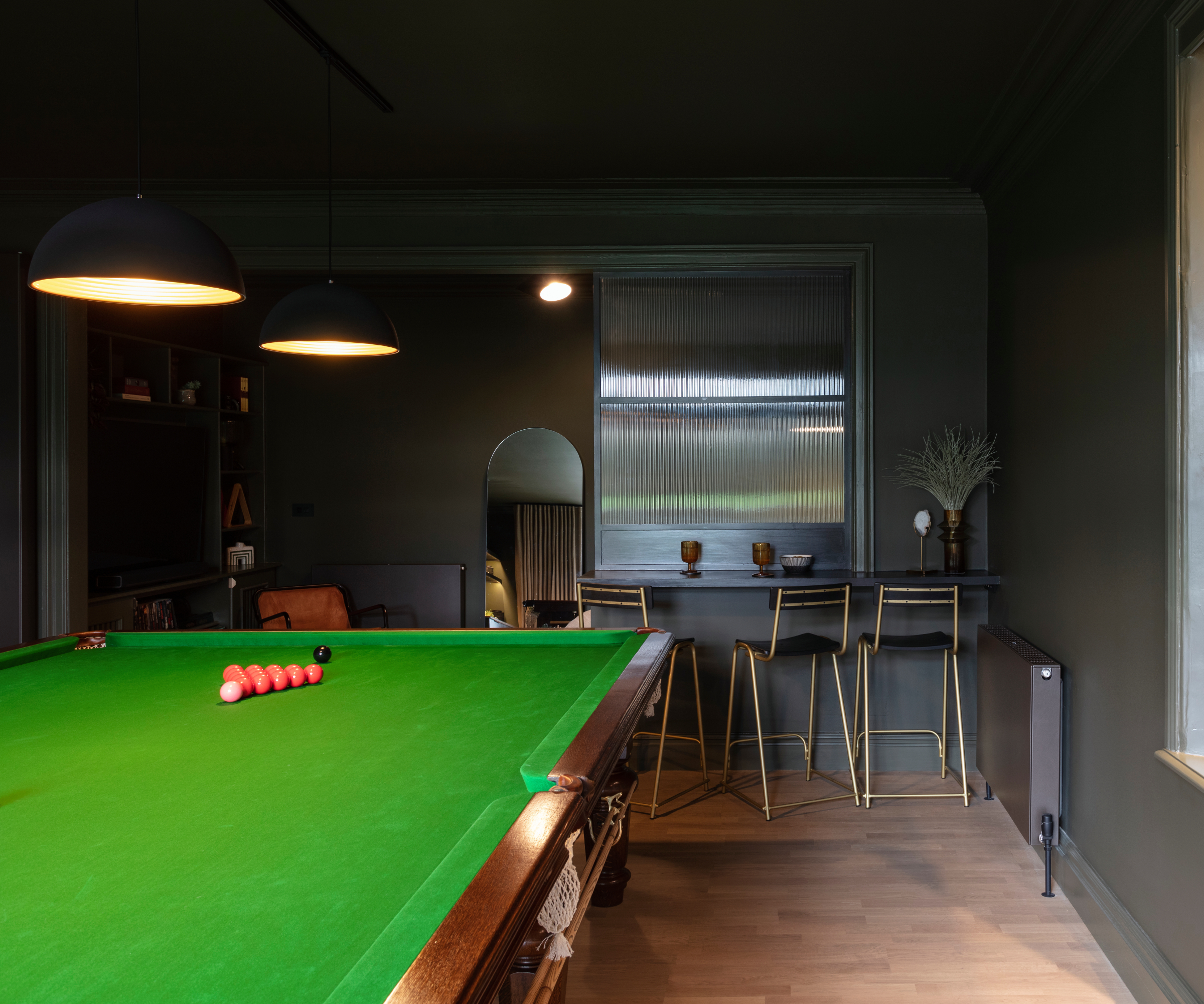 green topped pool table with glass screen divding gaming area with tv and sofas