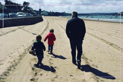 Older dad walking with two young boys on a beach