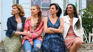 The sisters of Dreamland sitting on a garden wall in front of a house with graffiti sprayed on the windows. From left to right, they are Clare (Gabby Best), Leila (Aimee-Ffion Edwards), Mel (Lily Allen) and Trish (Freema Agyeman)