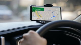 Nahaufnahme einer Person, der ein Auto fährt und sein Smartphone in der Hand hält, um mit der Google Maps App zum Ziel zu fahren