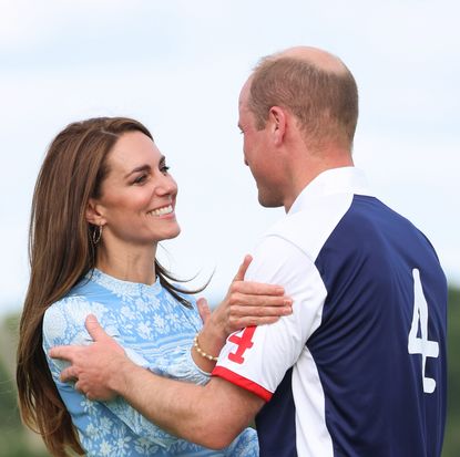 Kate Middleton wearing a blue dress and hugging Prince William who is wearing a a white and blue polo jersey