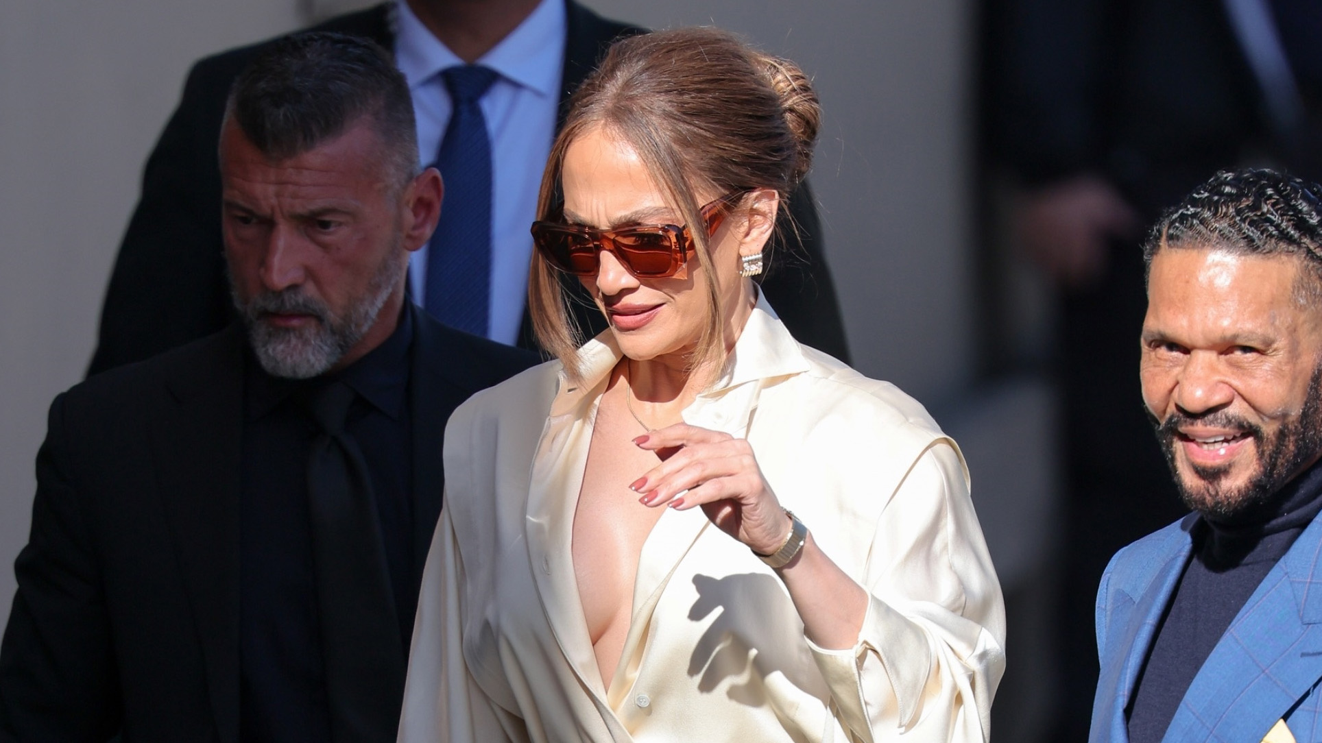 Jennifer Lopez wearing a white satin button-down blouse with wide-leg trousers and platform shoes, arriving at Jimmy Kimmel Live in Los Angeles