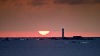 Winter Solstice sunset shows a pink sky behind a lighthouse. 