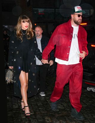 Taylor Swift wearing a black dress holding hands with Travis Kelce, wearing a red jacket and pants, walking outside at night