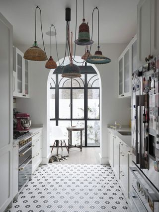 an all white kitchen in a home with an arrangement of 6 colorful pendant lights.