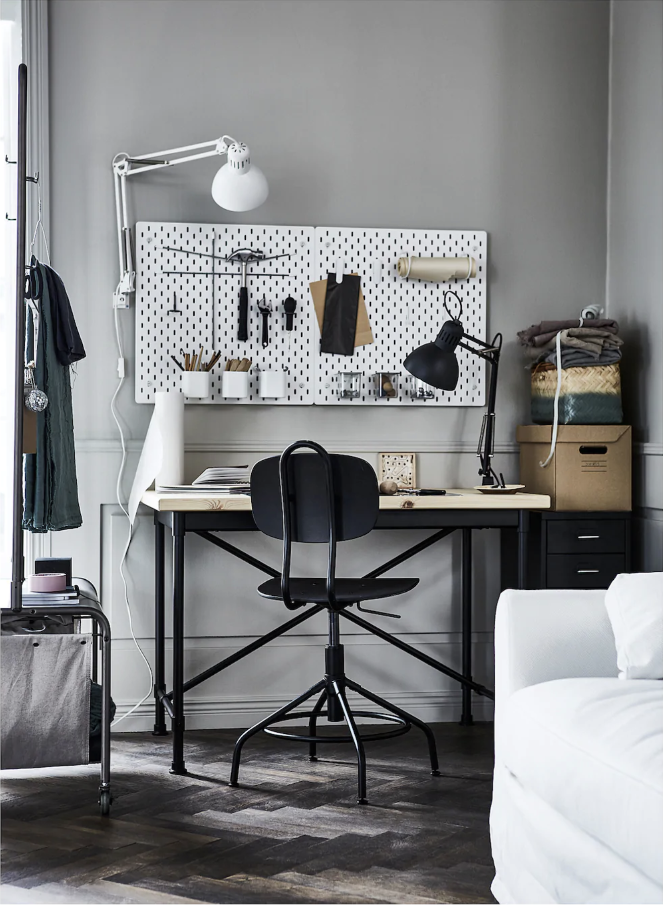 a monochrome office with a black desk and chair, a pinboard on the grey wall, a white lamp and gray hardwood floor