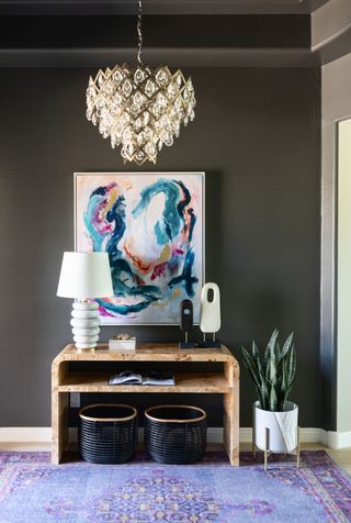 chocolate brown hallway/entryway with wooden console, chandelier, artwork and plant