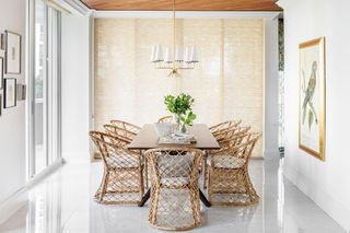 dining room with wooden table and rattan chairs white walls and glossy white floor tiles and parrot print on wall