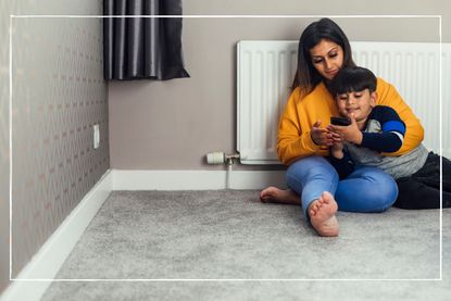 mother and son cuddling in front of a radiator looking at a mobile phone