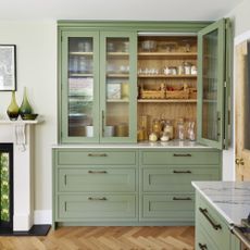 Sage green kitchen cupboard with glass doors containing kitchen essentials