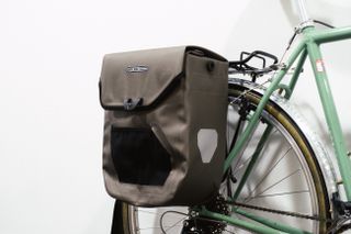 A brown boxy pannier mounted to a green bike against a white background