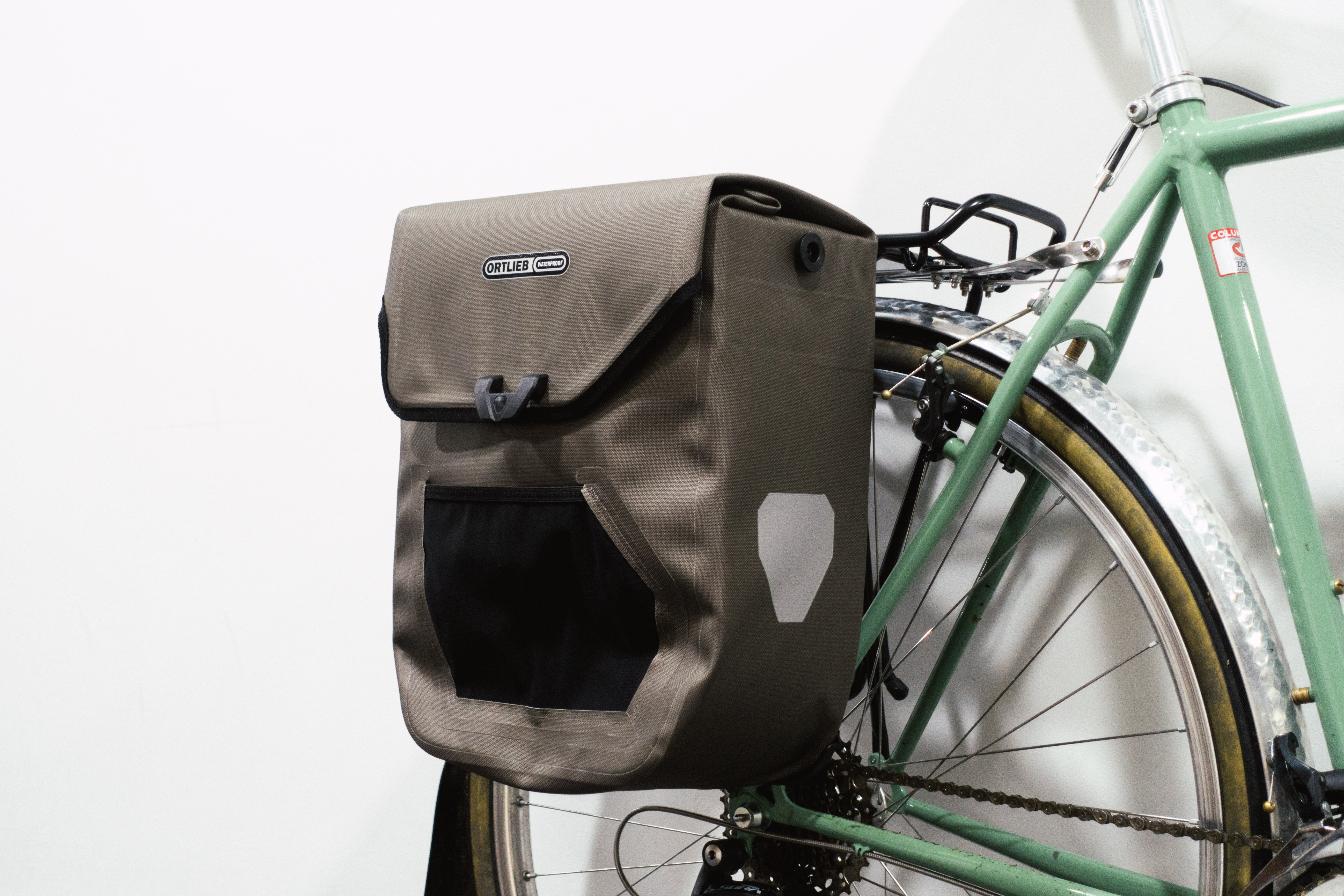 A brown boxy pannier mounted to a green bike against a white background