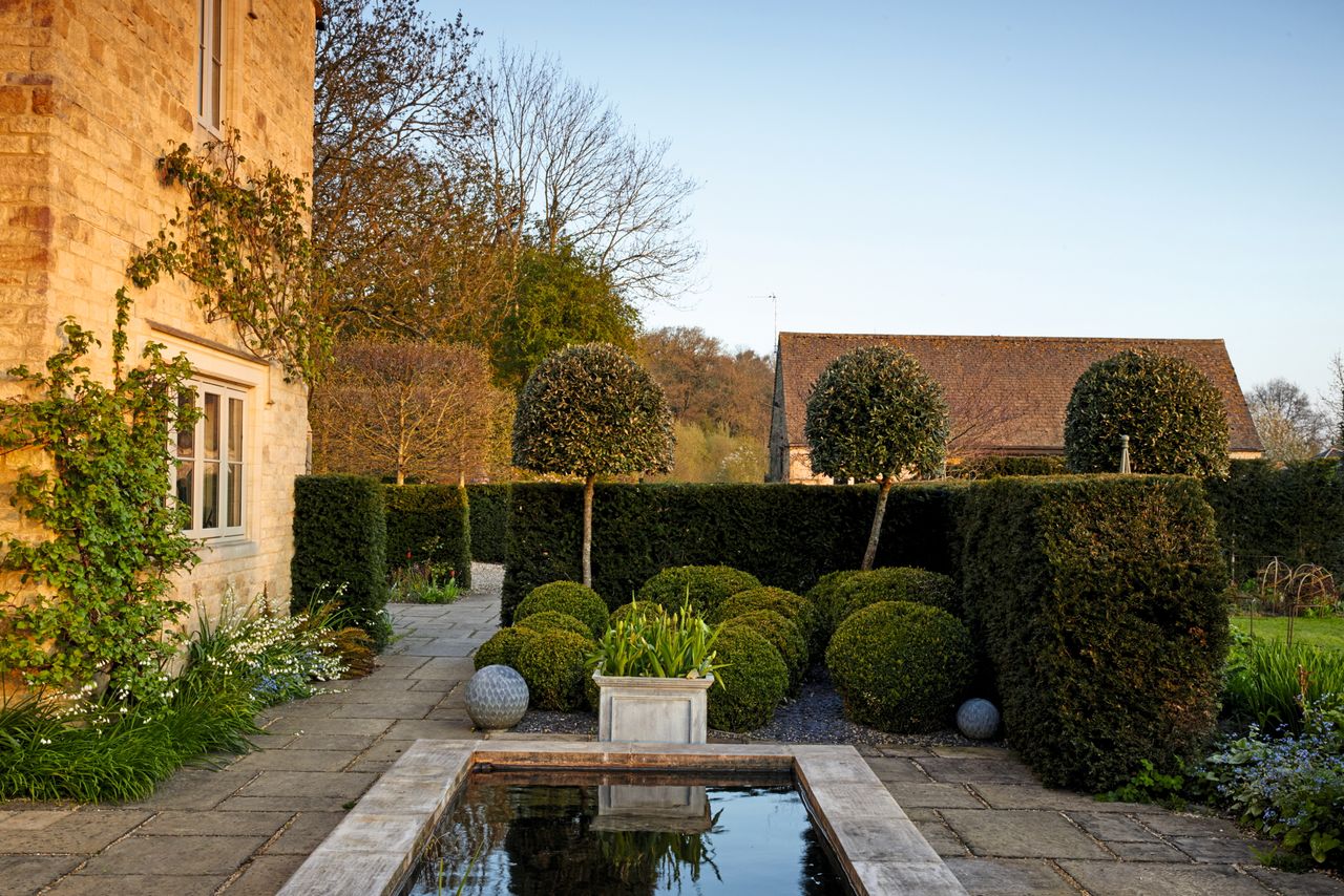 A formal pond by the house, with tightly cut box balls, yew and Quercus ilex.