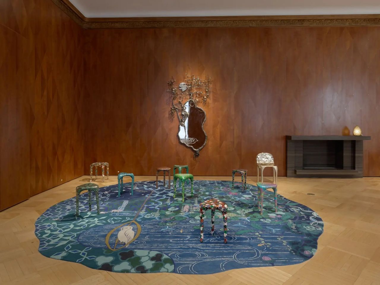 A seies of fantastical chairs, mirrors, and rugs is on display in a wooden-plastered gallery.