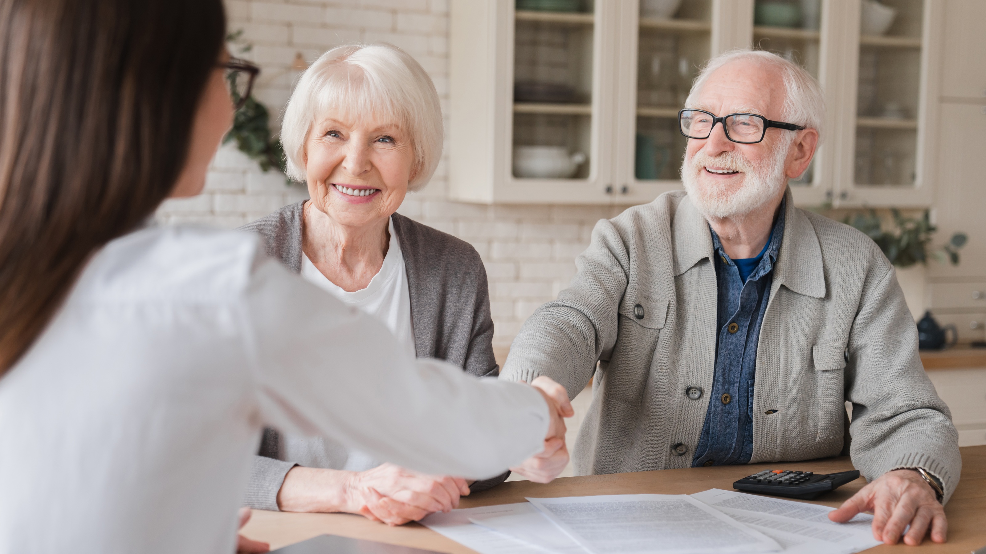 A financial adviser shakes hands with an older couple in her office.