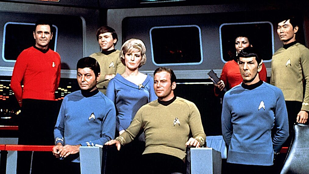 The crew of a futuristic starship in blue, red, and gold uniforms