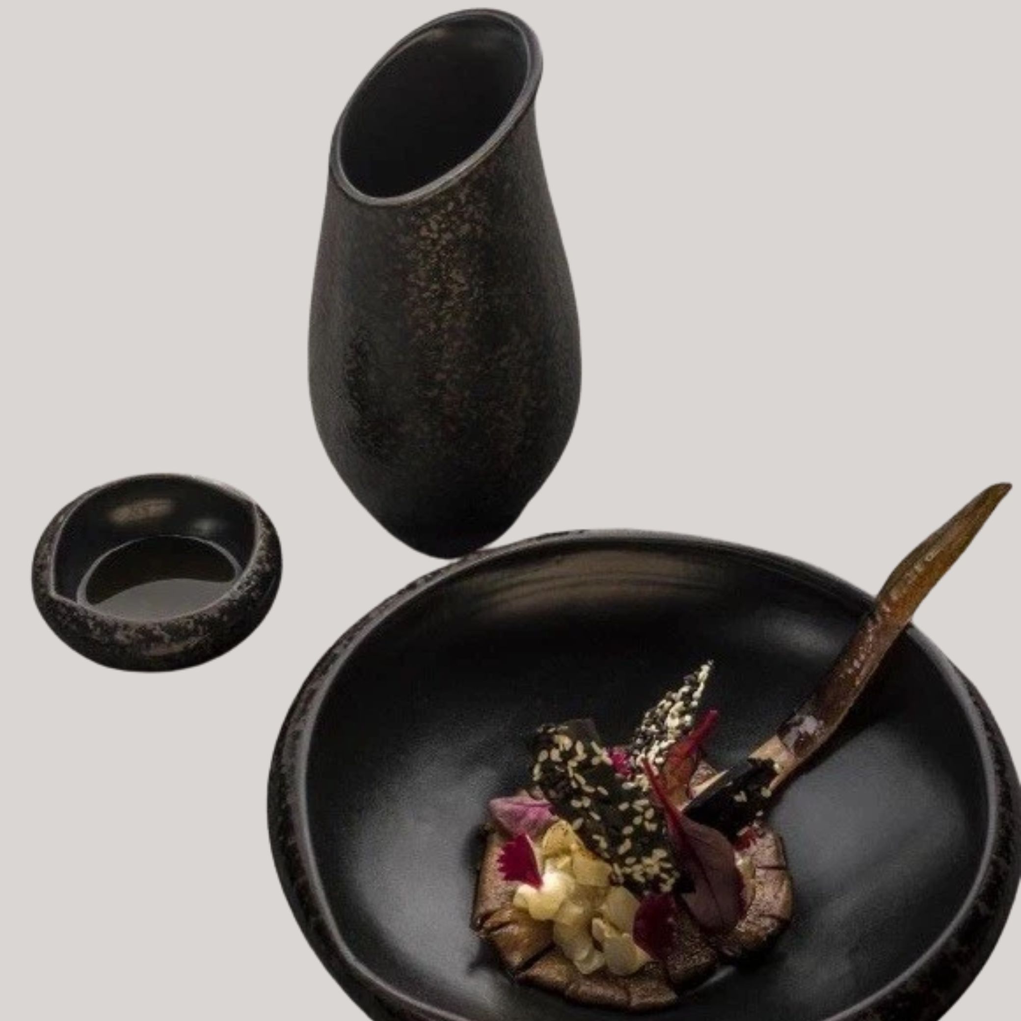 Black Satin Stone Gravy Boat placed along with two similarly designed plates on a pale gray background.