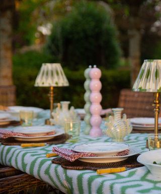 An outdoor dining table with a green and white tablecloth, green and pink salt and pepper shakers, and small green and white table lamps