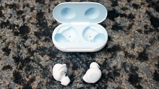 The Samsung Galaxy Buds in white next to their charging case on a grey surface
