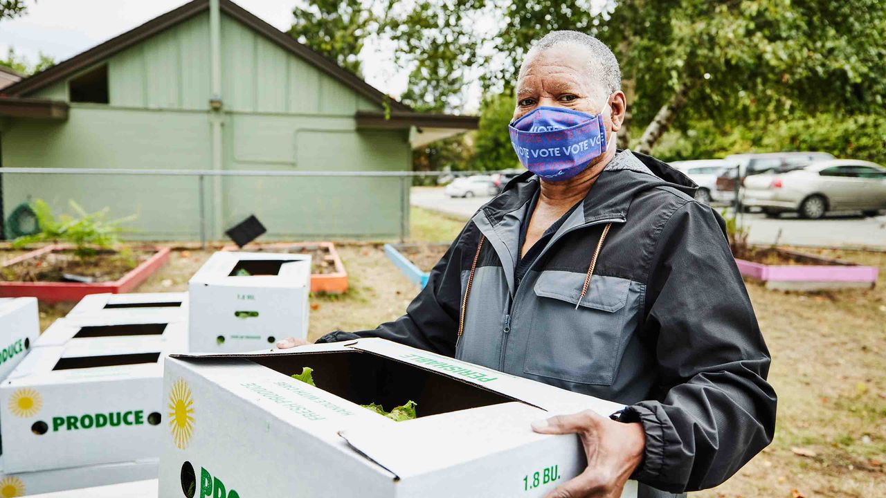 Photo of a man holding a box of produce wearing a mask that says &amp;quot;vote.&amp;#039;