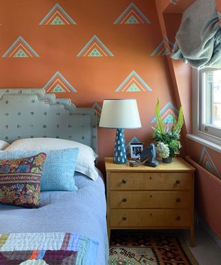 orange wallpaper, wooden chest of draws, blue bed