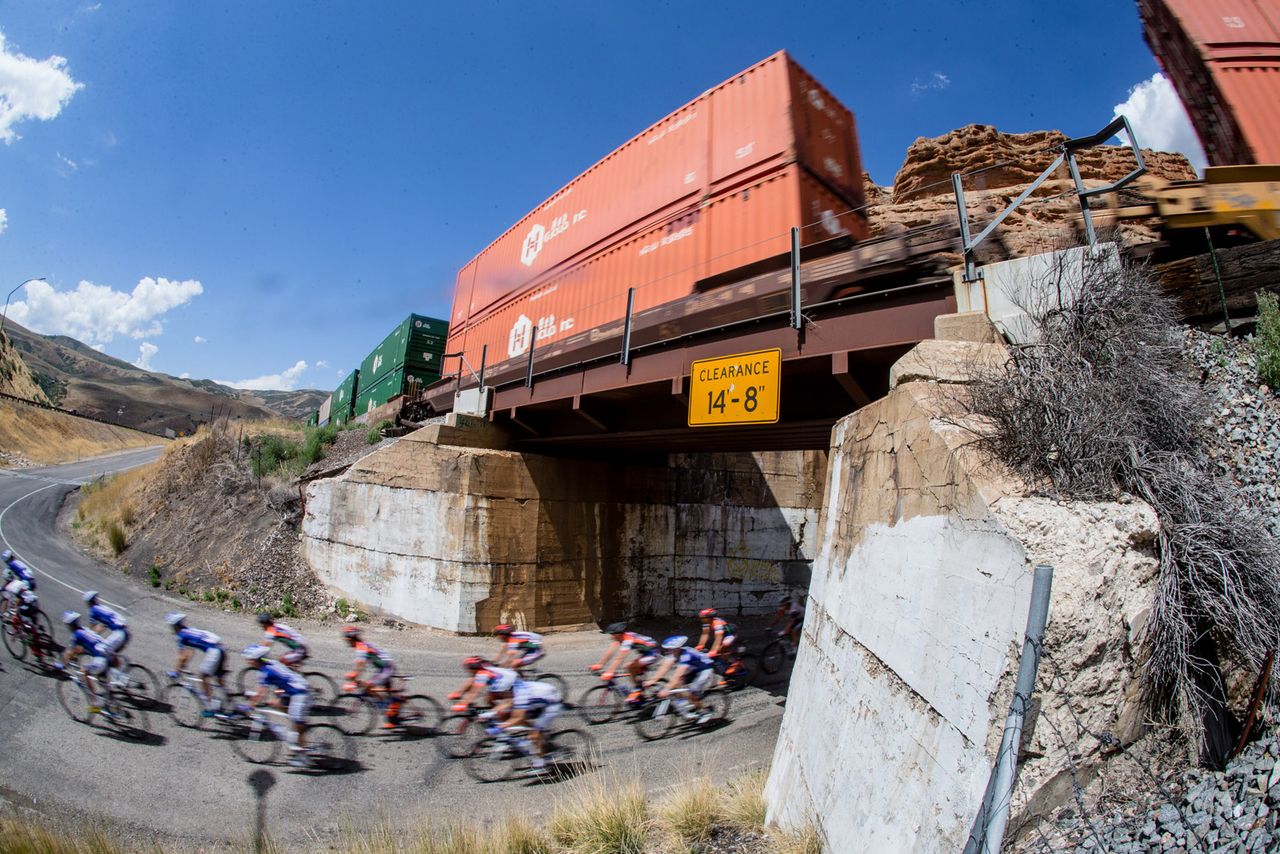 The peloton passes underneath a loaded train
